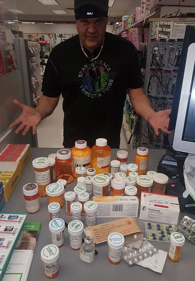 A man standing behind a table full of prescription drugs.